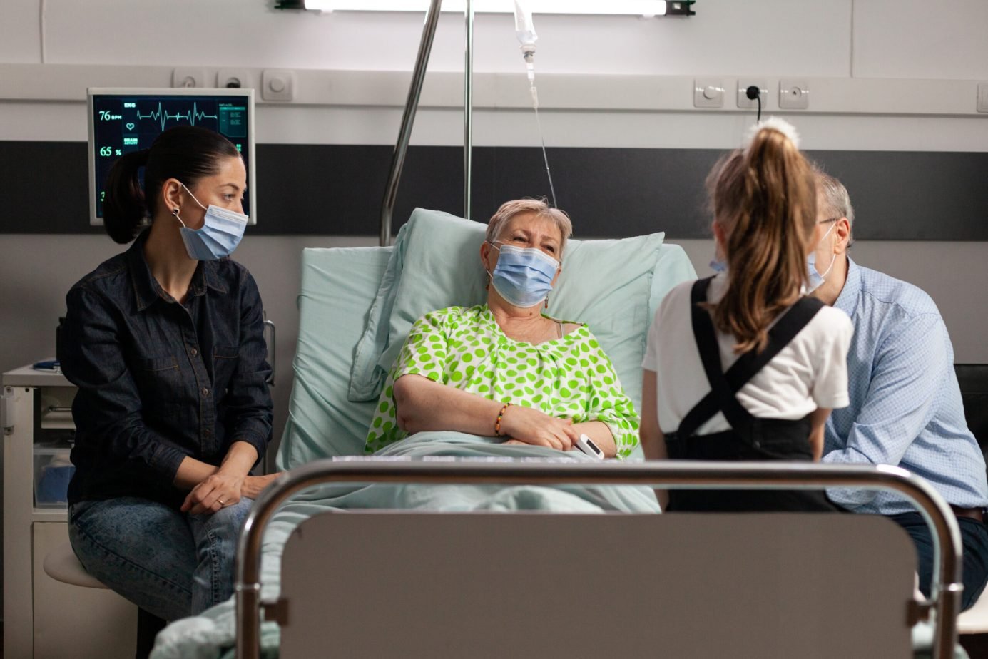 Family wearing protective face mask against covid19 while visiting sick grandmother in hospital ward. Senior pensioner woman resting in bed after medcial surgery waiting for healthcare treatment