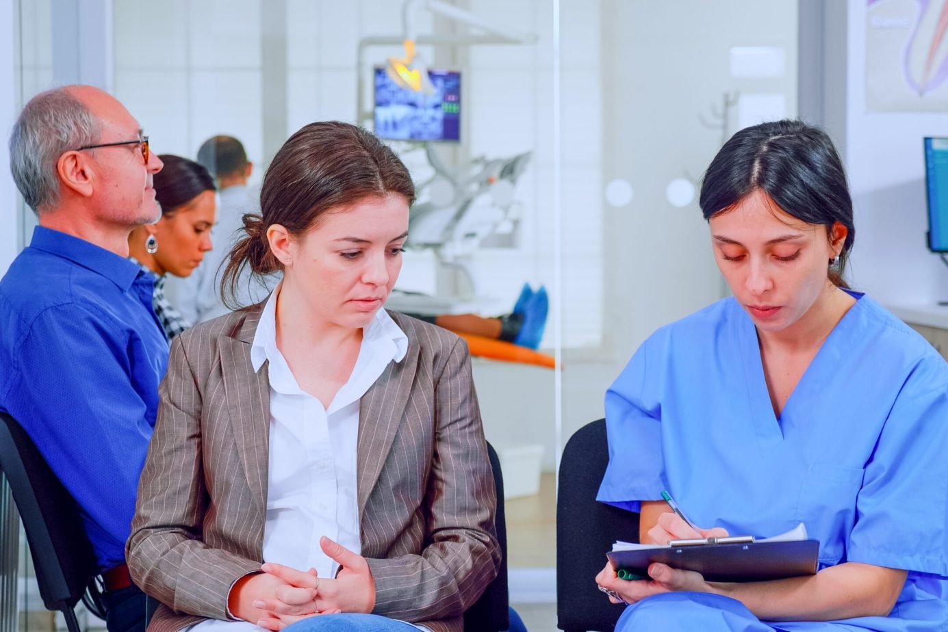 Nurse taking notes on clipboard about patient dental problems waiting for orthodontist sitting on chair in waiting room of stomatological clinic. Assistant explaining medical procedure to woman.